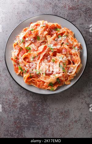 Le pappardelle alla Fiesolana sono un piatto cremoso e delizioso, preparato con pasta, pancetta, cipolla, pomodoro e formaggio, che si prepara nel piatto della tavola. Verticale Foto Stock