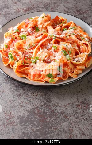 Le pappardelle alla Fiesolana sono un piatto cremoso e delizioso, preparato con pasta, pancetta, cipolla, pomodoro e formaggio, che si prepara nel piatto della tavola. Verticale Foto Stock