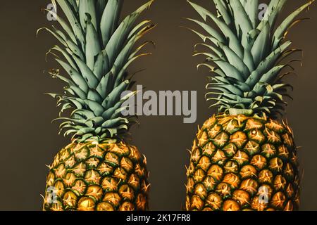 Un primo piano di due ananas interi freschi contro il muro scuro - sfondo cucina creativa Foto Stock