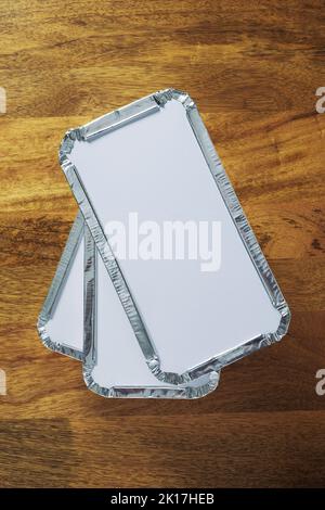 Pila di tre lamina argento vassoi da asporto shot da sopra il tavolo in legno top Foto Stock