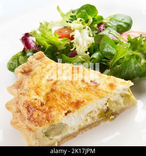 Una fetta di porri e formaggio di capra quiche su una piastra con croccante di insalata in foglie Foto Stock