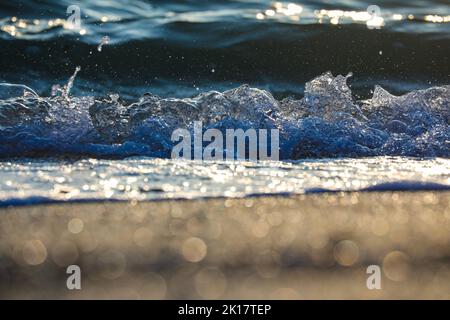 Closeup di schiantare l'onda dell'oceano sulla spiaggia. Onde di vonghi e mare dolce surf. Effetti di luce bokeh con messa a fuoco morbida in primo piano. Fotografia dell'ora d'oro. Foto Stock