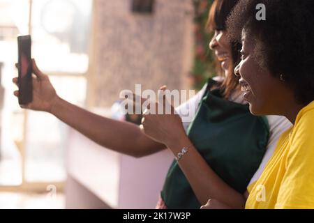 le donne africane in un salone che controlla i loro telefoni eccitati Foto Stock