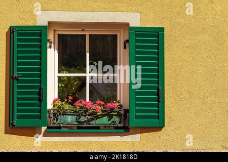 Finestra con persiane in legno verde e fiori di geranio rosso. Piccolo villaggio di Malborghetto-Valbruna in Val canale, Udine, Friuli-Venezia Giulia, Italia. Foto Stock