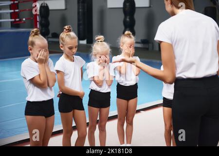 Formazione con il coach. Giovane donna che insegna le bambine, atleti di ginnastica per principianti ad allenarsi in palestra sportiva, al coperto. Concetto di sport Foto Stock