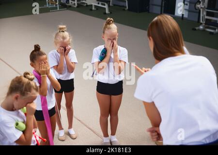 Formazione con il coach. Giovane donna che insegna le bambine, atleti di ginnastica per principianti ad allenarsi in palestra sportiva, al coperto. Concetto di sport Foto Stock