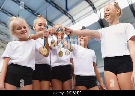 Ragazze felici, atleti di ginnastica femminile che mostrano le loro medaglie alla macchina fotografica alla palestra sportiva, al coperto. Concetto di vittoria, sport, studio, realizzazioni Foto Stock