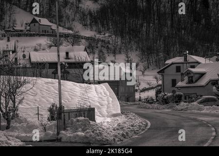 Una scala di grigi di case rurali lungo la strada in inverno Foto Stock