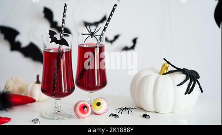 Primo piano di due sanguinosi cocktail calici di vetro per Halloween, bottiglia forma cranio, occhi caramelle, pipistrelli, zucche sfondo bianco. Concetto di arredamento per Hal Foto Stock