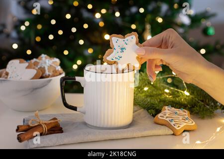 donna immersione mano decorato fiocco di neve biscotto di pan di zenzero in tazza di bevanda calda Foto Stock