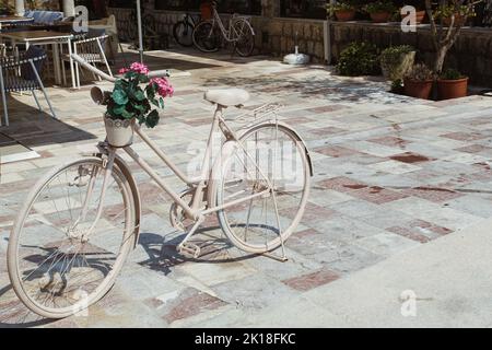 Bicicletta d'epoca bianca con cesto di fiori isolato su sfondo bianco nella città vecchia, Perast, Montenegro. Foto Stock