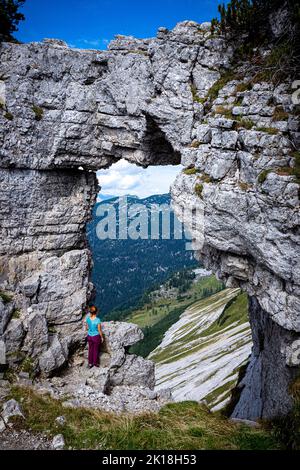 Escursionista femminile che gode della vista attraverso la cosiddetta Loserfenster, un arco di roccia sul monte Loser, Ausseer Land, Stiria, Austria Foto Stock