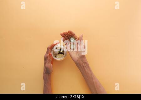 vista dall'alto delle monete a risparmio di mano delle donne anziane in un vaso Foto Stock
