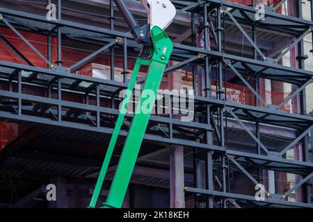 Il sollevatore del braccio si trova contro i ponteggi intorno alla costruzione dell'edificio Foto Stock