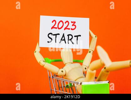 2023 simbolo di avvio. White paper con parole 2023 Start, modello umano nel carrello. Bella tavola arancione sfondo arancione. Business e 2023 inizio conce Foto Stock