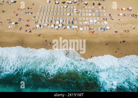 riprese aeree da un drone su una spiaggia di sabbia con persone che prendono il sole e rilassarsi. Vista piatta della costa e delle onde turchesi del surf e della gente Foto Stock