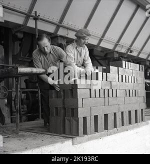 Anni '1950, storico, due lavoratori maschi, uno che indossa un berretto piatto, impilando mattoni appena cotti alla London Brick Company, Bedford, Inghilterra, Regno Unito. Foto Stock