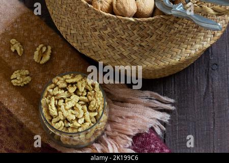 Noci intere e un nutcracker in un cesto, nocciole in un vaso su un tavolo di legno. Foto Stock