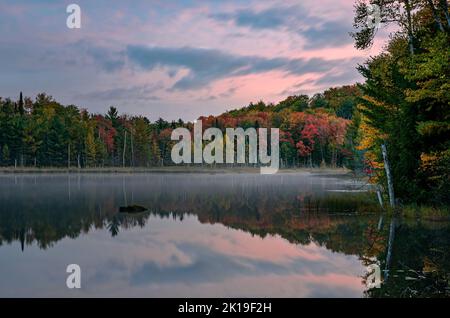 Le nuvole rosa illuminate all'alba rompono il cielo blu sul lago Council nella foresta nazionale di Hiawatha nella contea di Alger, Michigan Foto Stock