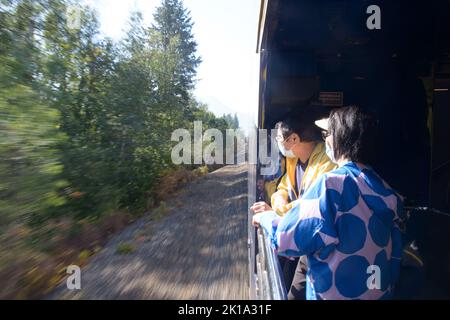 Coppia asiatica sul vestibolo del treno Rocky Mountaineer che guarda il paesaggio delle Montagne Rocciose Canadesi Foto Stock