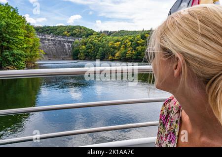 Bella ragazza che guarda la diga di String of Lights sulla cima di una barca che viaggia attraverso il lago Rursee, nel mezzo del Parco Nazionale di Eifel, circondato Foto Stock