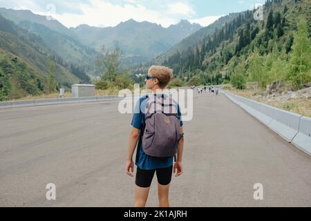 Giovane viaggiatore con uno zaino sulla strada godendo di vista sulle montagne. Foto Stock