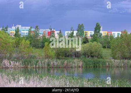 Lo stagno della città costruito per catturare le acque piovane, migliorare la qualità dell'acqua e prevenire le inondazioni fornisce anche un parco urbano. Alberta Children's Hospital sul retro. Foto Stock