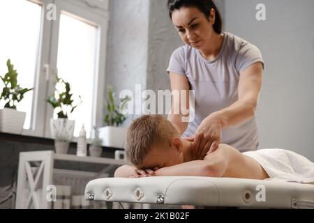 il massaggiatore dona al bambino un massaggio alla schiena. Massaggio bambini. Massaggio terapista con massaggio spalle di 7 anni. Terapia fisica Foto Stock
