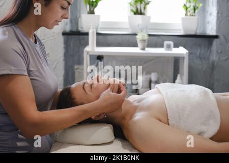 massaggio viso con olio in stile tradizionale realizzato da donne di bellezza professionisti. massaggio anti-età Foto Stock