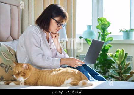 Donna con gatto seduto a letto a casa, donna che utilizza un computer portatile Foto Stock