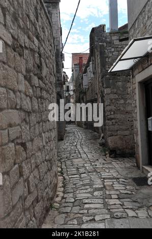 Foto verticale di uno stretto vicolo di ciottoli a Trogir, Croazia. Foto Stock