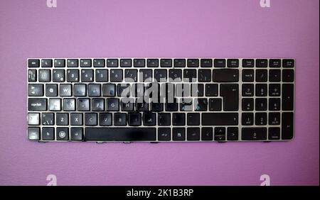 Tastiera del notebook usurata e rotta su sfondo viola Foto Stock