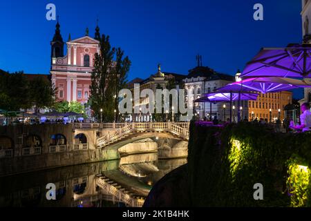 Città di Lubiana di notte in Slovenia, ponte triplo illuminato sul fiume Lubiana e Chiesa Francescana dell'Annunciazione. Foto Stock