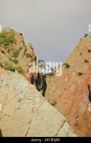 Uno scatto verticale di una chiesa ortodossa vista tra montagne rocciose in una giornata nuvolosa Foto Stock