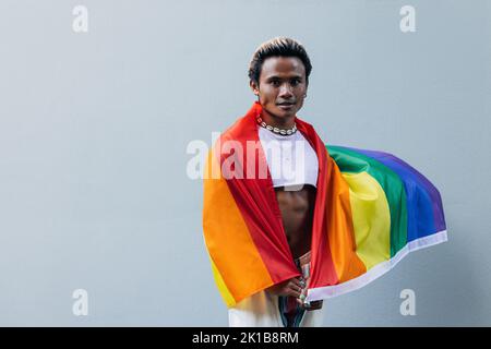 Ritratto di un giovane ragazzo con bandiera lgbt in posa all'aperto sulla parete grigia Foto Stock