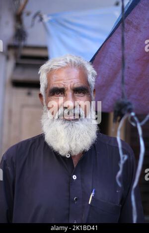 Un ritratto verticale di un vecchio maschio pakistano con una barba bianca in una kurta in piedi per strada Foto Stock