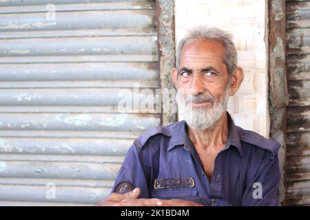 Un fuoco poco profondo di un vecchio maschio pakistano con una barba bianca che si erge contro un muro nella strada Foto Stock