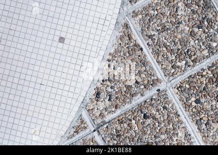 Metà delle piccole piastrelle di ceramica squadrate bianche e sporche e la struttura e il motivo del pavimento in pietra di ciottoli marrone vecchio, mosaico retrò, superficie ruvida urbana, Foto Stock