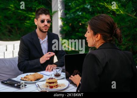 I giovani uomini d'affari fanno colazione insieme e cercano di fare un affare sul loro ultimo progetto Foto Stock