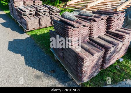 Vecchie scandole del tetto smontate dopo la sostituzione impilate ordinatamente su pallet in luce laterale soleggiata con ombre. Foto Stock