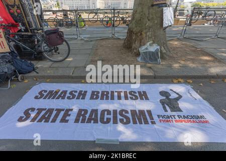 Westminster, Londra, Regno Unito. 17 settembre 2022. Un audace striscione di protesta disposto sul marciapiede vicino a un albero in un ambiente urbano del Regno Unito. Lo striscione recita: “SMASH BRITISH STATE RAZZISM! COMBATTERE IL RAZZISMO COMBATTERE L'IMPERIALISMO" in lettere maiuscole nere e rosse, accompagnate da una sagoma di pugno rialzato. Biciclette e barricate metalliche sono visibili sullo sfondo, suggerendo una manifestazione pubblica o un raduno di attivisti. Protesta fuori New Scotland Yard per Chris Kaba, un uomo nero di 24 anni che è stato ucciso dalla polizia Penelope Barritt/Alamy Live News Foto Stock