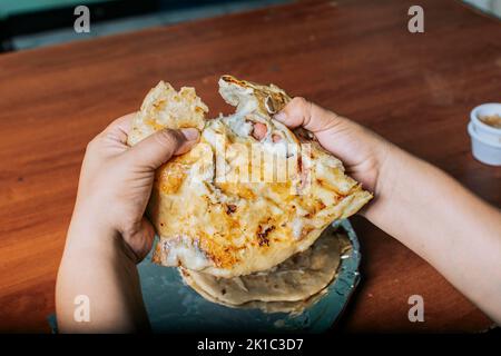 Vista delle mani che dividono le deliziose pupusas Salvadoran su un tavolo di legno. Concetto di pupe tradizionali fatte a mano, le mani che dividono il delizioso Nicaraguan Foto Stock