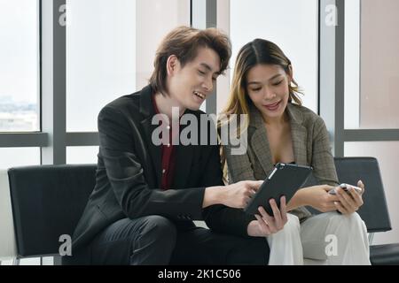 Felice uomo e donna asiatico busimess guardando il telefono cellulare per rilassarsi dopo il lavoro in ufficio Foto Stock