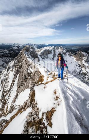 Arrampicatore su una cresta rocciosa innevata, dietro il crow di picco, vista del panorama di montagna, escursioni a Ammergauer Hochplatte, in autunno, Alpi Ammergau, Baviera Foto Stock