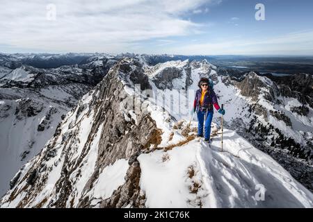 Arrampicatore su una cresta rocciosa innevata, dietro il crow di picco, vista del panorama di montagna, escursioni a Ammergauer Hochplatte, in autunno, Alpi Ammergau, Baviera Foto Stock