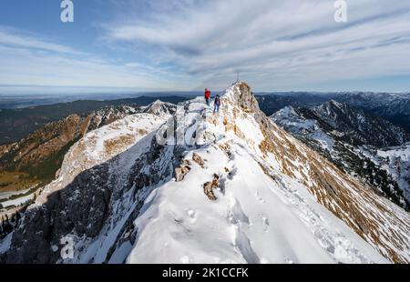 Due scalatori su una stretta cresta rocciosa innevata, cima del Hochplatte Ammergauer con la croce sommitale, vista del panorama montano, escursioni in autunno Foto Stock