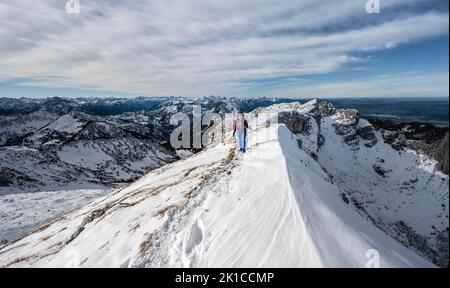 Arrampicatore su una cresta rocciosa innevata, sentiero escursionistico per Ammergauer Hochplatte, vista del panorama montano, dietro il crow di picco, in autunno, Alpi Ammergau Foto Stock