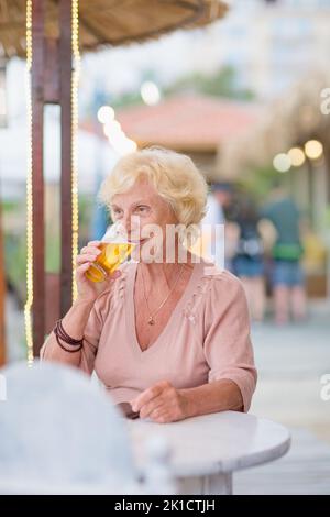 Donna matura seduta a un tavolo in un bar estivo e bere birra Foto Stock