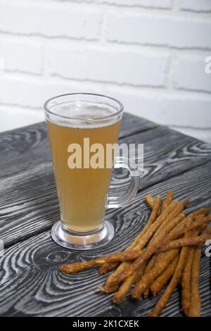 Salsicce sottili per birra. Nelle vicinanze si trova un bicchiere di birra di grano. Sfondo da tavole di pino. Primo piano. Foto Stock