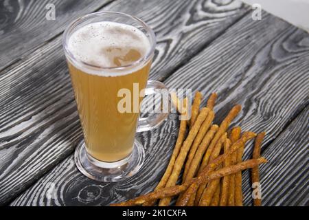 Salsicce sottili per birra. Nelle vicinanze si trova un bicchiere di birra di grano. Sfondo da tavole di pino. Primo piano. Foto Stock